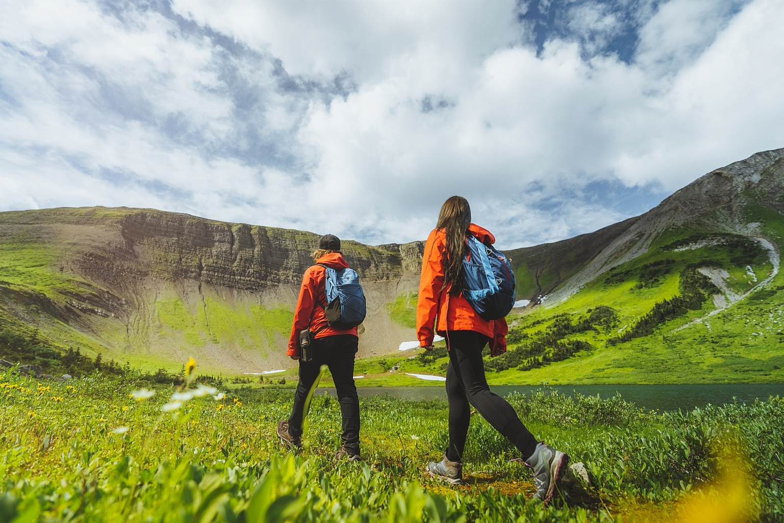 Two people wearing orange shirts walking through lush alpine meadows at Windfall Lake in Tumbler Ridge.