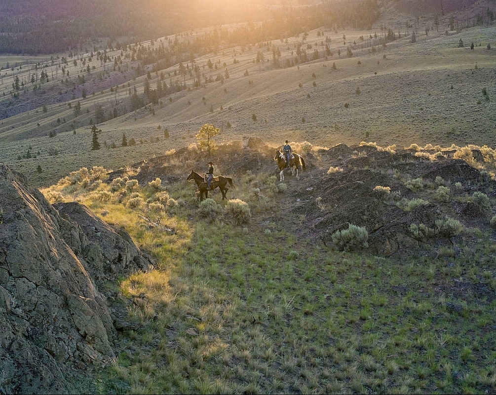 Two people on horseback riding through the sagebrush-covered hills.